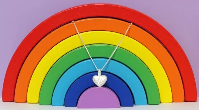 Ascheschmuck-Herzkette „Emmi“ mit Regenbogen-Motiv aus 925er Sterling-Silber vor einer Regenbogendekoration (nicht im Lieferumfang enthalten)