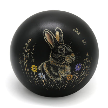 Schwarze Keramik-Tierurne in Kugelform mit handgemaltem Kaninchenporträt und Blumenfeld