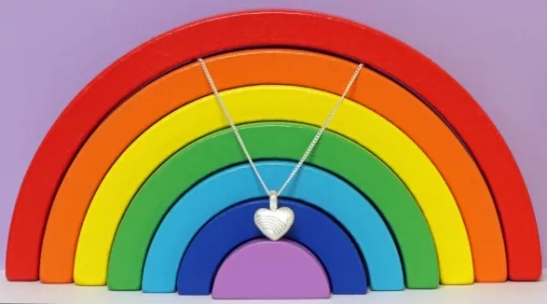 Ascheschmuck-Herzkette „Emmi“ mit Regenbogen-Motiv aus 925er Sterling-Silber vor einer Regenbogendekoration (nicht im Lieferumfang enthalten) Ascheschmuck-Herzkette „Emmi“ mit Regenbogen-Motiv aus 925er Sterling-Silber vor einer Regenbogendekoration (nicht im Lieferumfang enthalten)